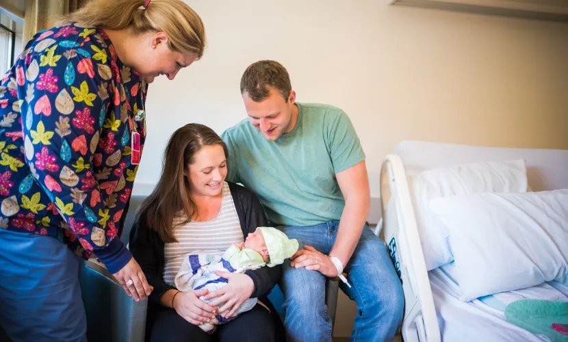 New mother and father holding child with nurse