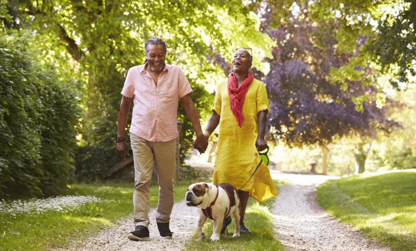 An older couple walks outside with a dog on a spring day