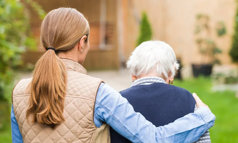 A woman walks with her arm around her older mother as they enjoy spending time together.