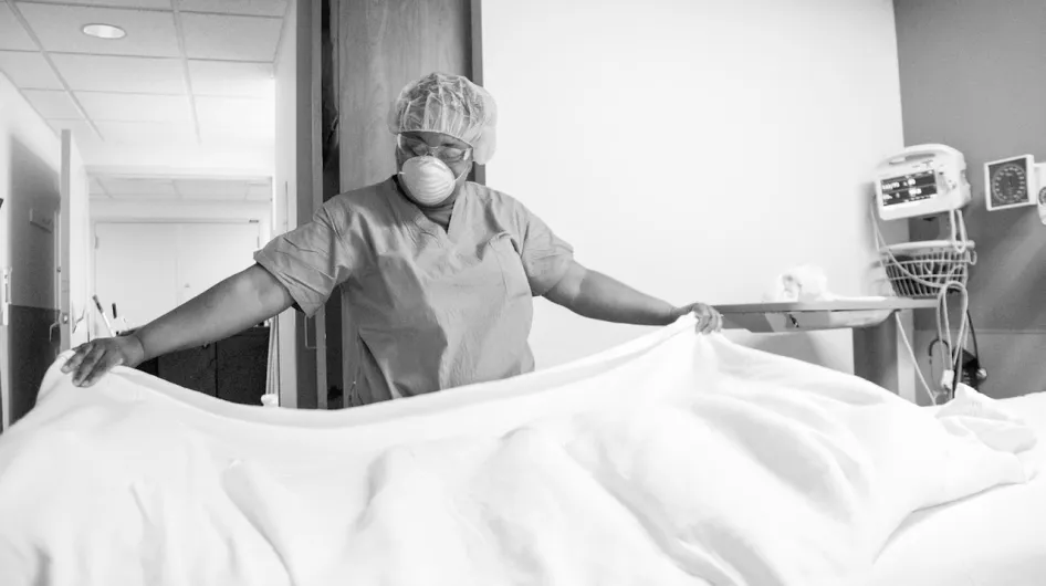 A housekeeper in a face mask makes a bed at South Shore Hospital
