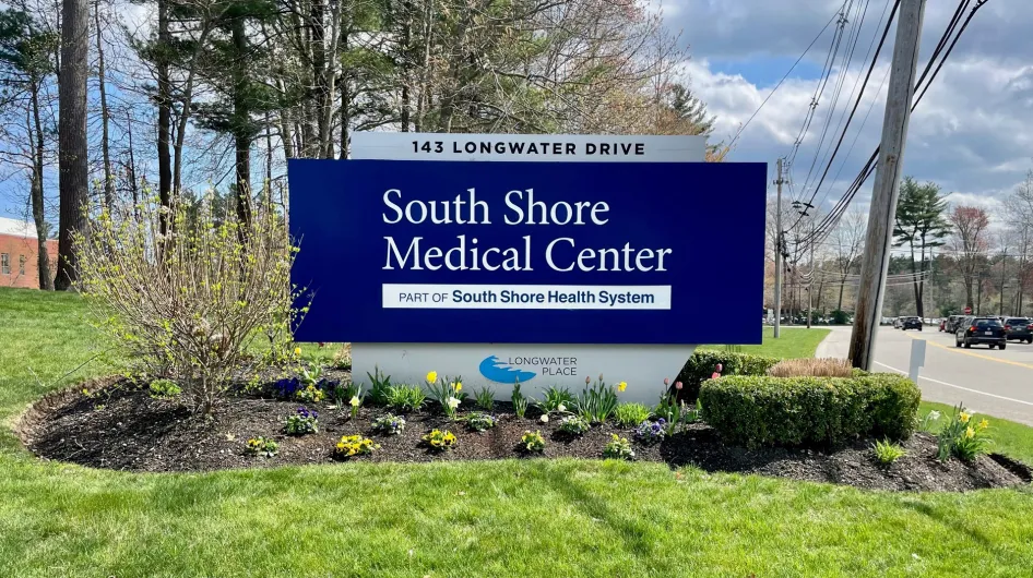 The exterior sign at South Shore Medical Center Norwell, featuring green shrubs, tulips, and other colorful spring foliage
