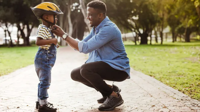 A father checks his young son's bike helmet before he goes for a bike ride.