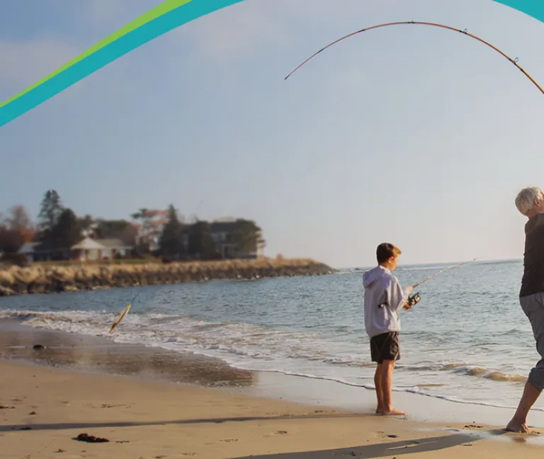A man and his grandson fish near the edge of the water at the beach
