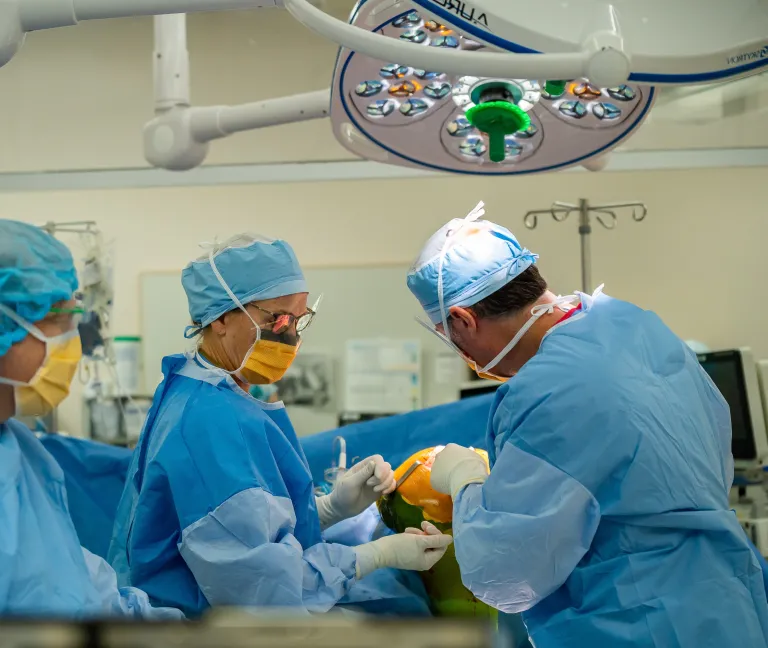 Three surgeons wearing blue scrubs, caps, and gloves crowd around a patient during a surgical procedure at South Shore Health