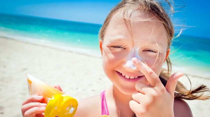 Smiling girl putting sunscreen on her nose.
