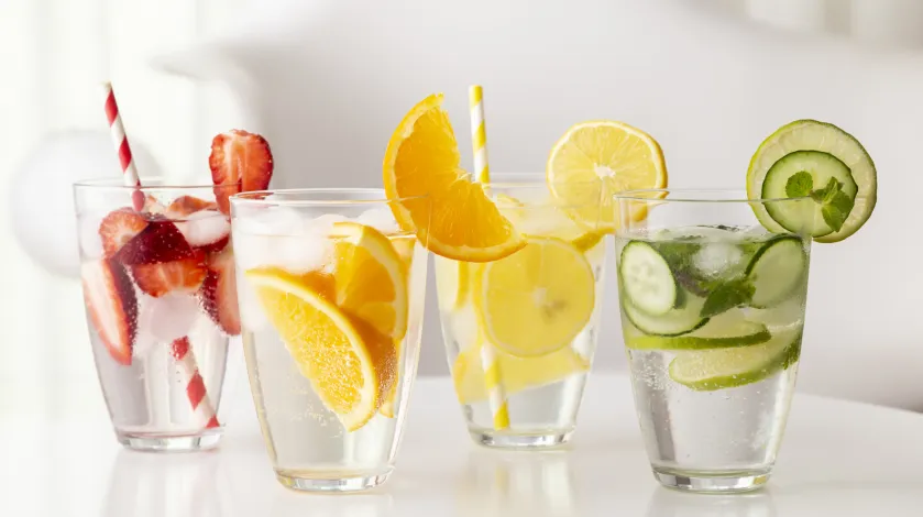 Four glasses of water infused with fruit and vegetables, including strawberries, citrus and cucumber