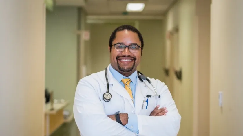 Khalil Alleyne, MD smiles for a portrait in his lab coat.