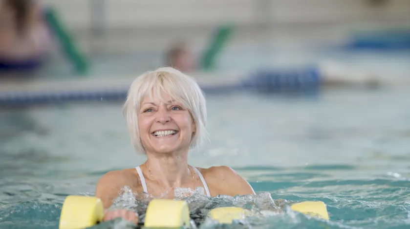 Older woman smiling as she's doing aquatic therapy in a pool