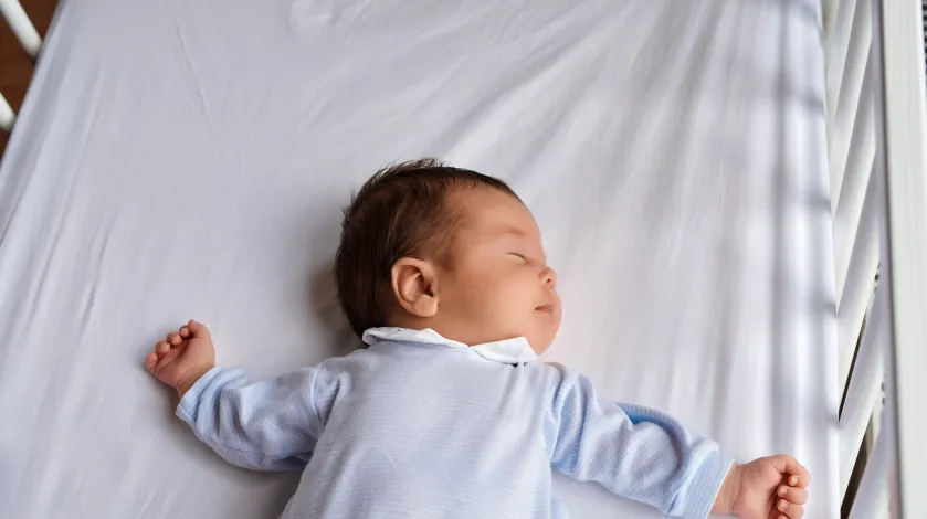 A baby sleeps on his back in an empty crib safe sleep