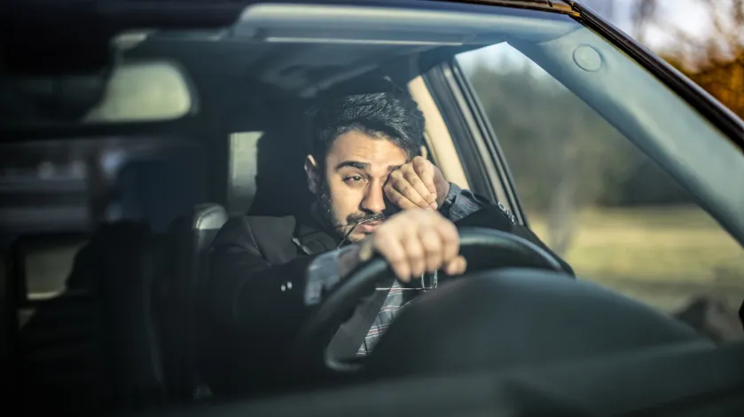 A man yawns while behind the wheel of his car as he experiences drowsy driving