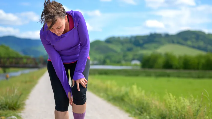 A woman stops to check her sore knee while out for a run in a scenic setting