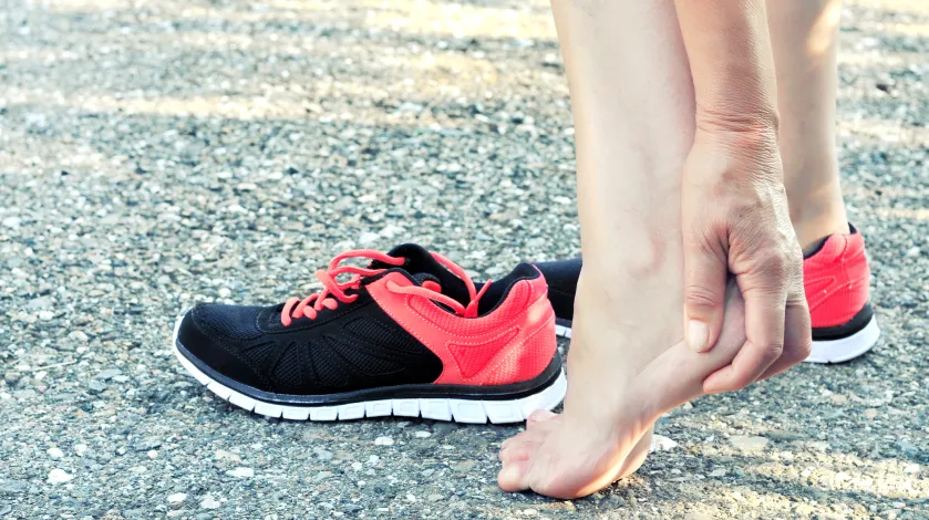 A woman rubs her heel after taking off her running shoes due to heel pain