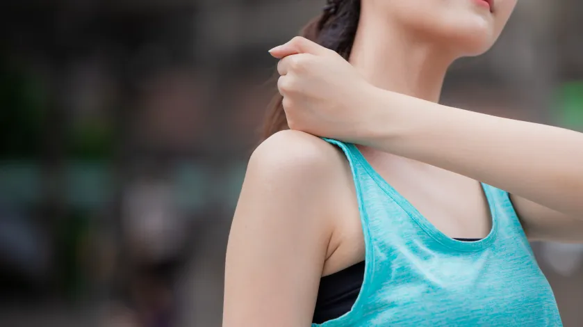 A woman in gym clothes rubs near her shoulder after experiencing pain while exercising