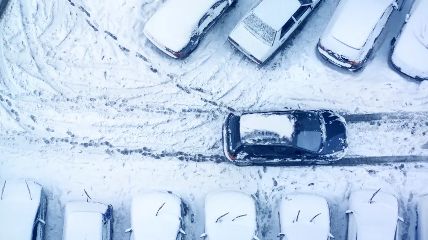 An overhead view of a car driving in a snowy parking lot