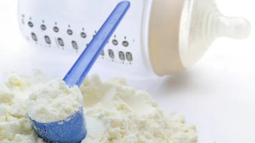 A spoonful of powdered infant formula with an empty baby bottle in the background