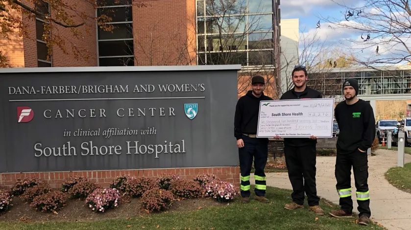 Employees from Express Towing stand in front of the Cancer Center with a donation check.