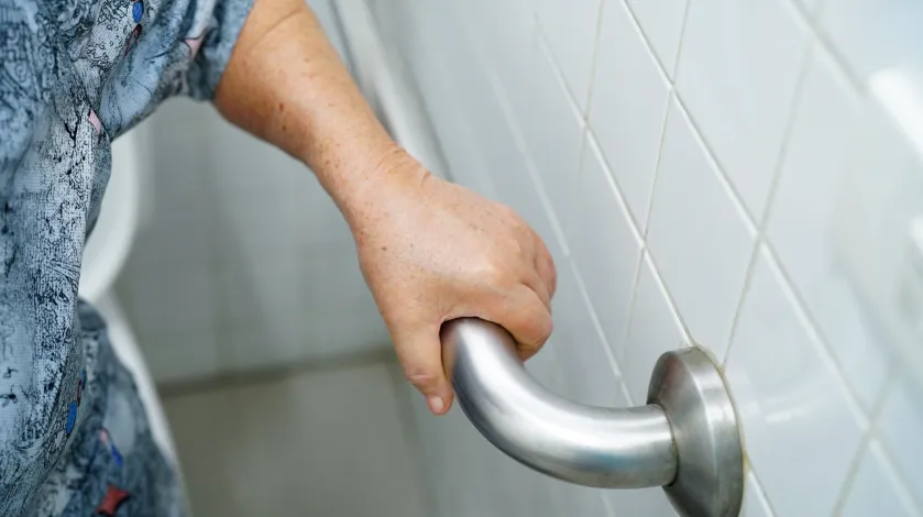 A close up of the hand of an older woman holding on the a grab bar in her bathroom for prevent falling