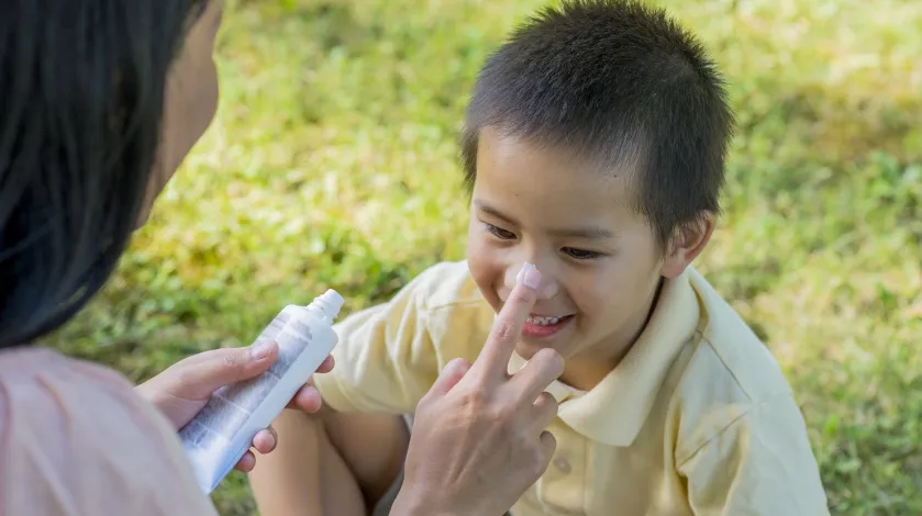 A mom applying sunscreen to her son's nose and face