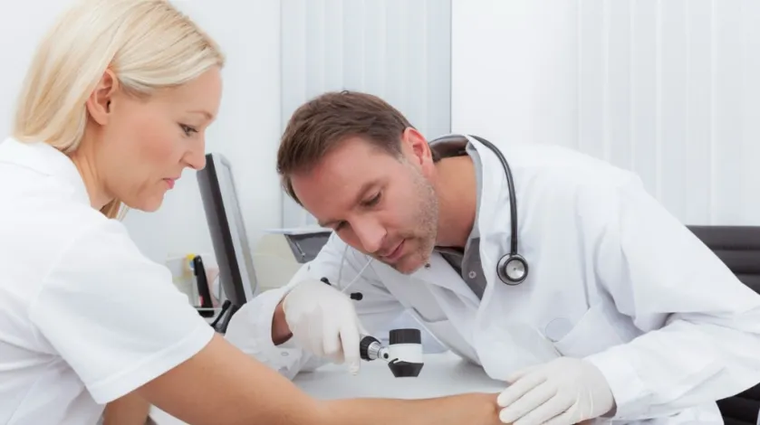 A dermatologist does a skin cancer screening on a female patients arm