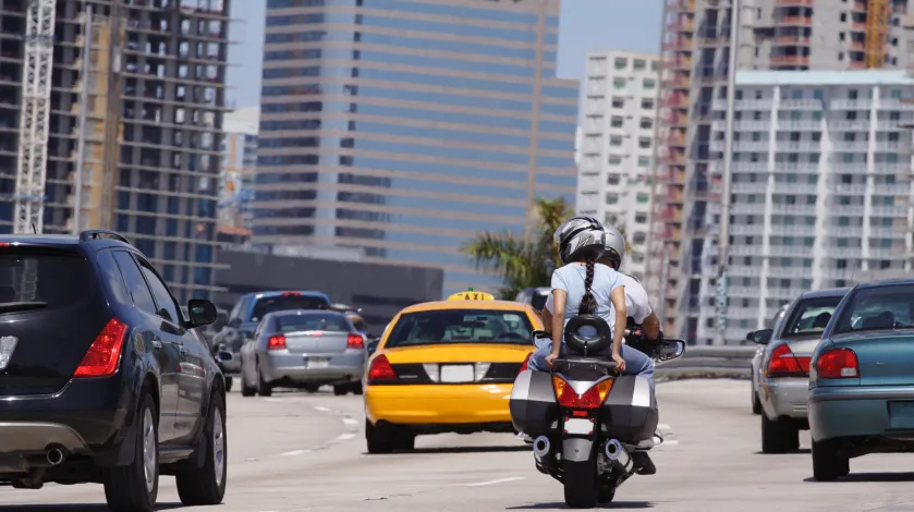 Two riders on a motorcycle on a the highway, with other cars around them in normal traffic.