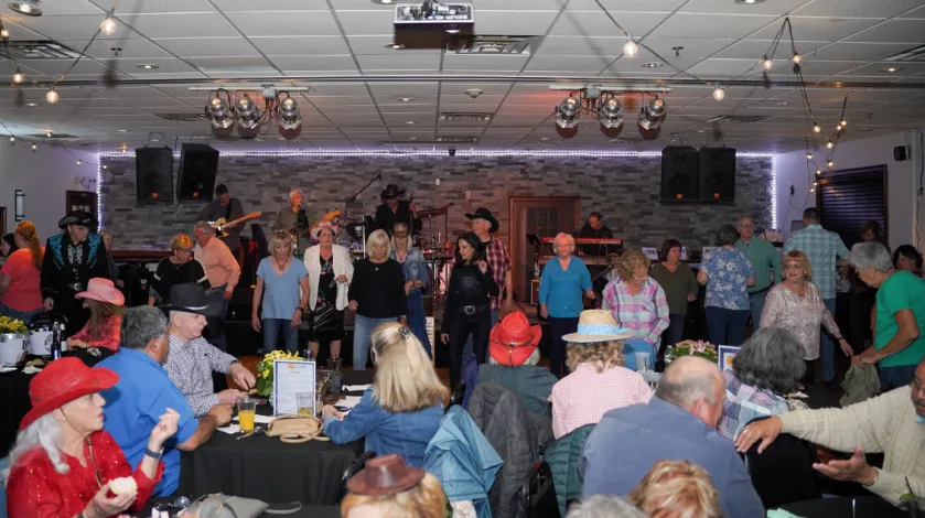 A panoramic view of the crowd at Kickin' Up Country 2023, featuring people line dancing and seated wearing western-themed attire.