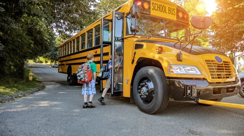 Two children wait in line to get on a school bus as it stops on a suburban street