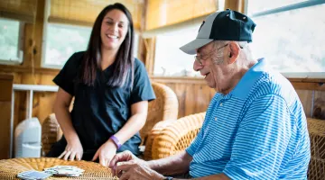 Older man smiling and playing cards with younger nurse