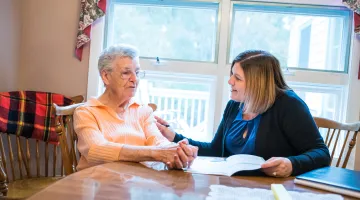 Young woman speaking with elderly woman as they review a book