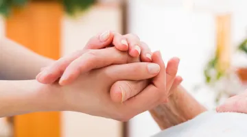 A pair of hands clasped around an older person's hand