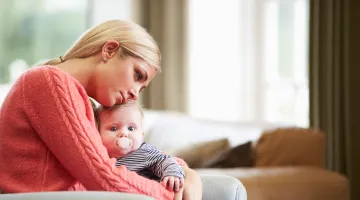 A new mom holding her baby and looking sad