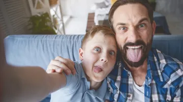 A child and his father laugh and make funny faces together while looking into the camera