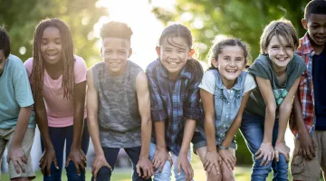 A group of kids poses smiling while playing outside in the summer