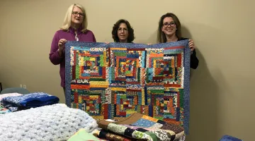Tammie Ryan, RN, Shirley MacLeod of Thimbles and Friends, and Lisa Royer pose with a quilt