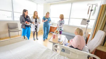 A group of clinicians gather in a sunny patient room.