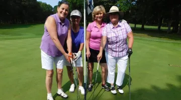 A group of women with clubs pose at a golf hole