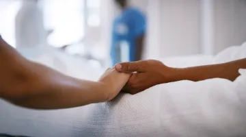 A person holding a patient's hand in a hospital bed providing comfort to the patient