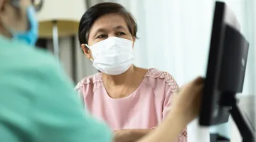Asian woman wearing a face mask talks to her doctor while looking at a computer screen