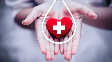 A knitted red heart with a white cross being held in two hands to show thanks for blood or plasma donations