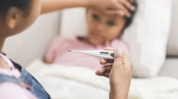 A mother looks at a thermometer with her hand on her child's forehead.