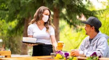 A masked waitress talks to a patron at an outdoor restaurant