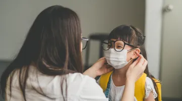 A mother helps her young daughter put on a face mask before heading to school