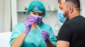A provider puts a COVID-19 swab into a test tube as a patient watches