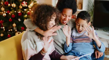 A family gathers around a tablet in front of a Christmas tree to have a video call with loved ones during COVID-19.