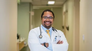 Khalil Alleyne, MD smiles for a portrait in his lab coat.