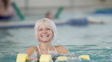 Older woman smiling as she's doing aquatic therapy in a pool