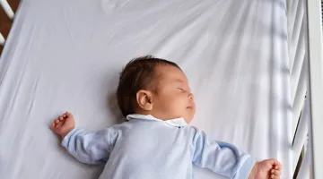 A baby sleeps on his back in an empty crib safe sleep