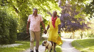An older couple walks outside with a dog on a spring day