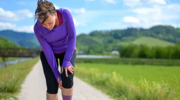 A woman stops to check her sore knee while out for a run in a scenic setting