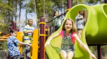 A group of school-age children happily plays together on a playground jungle gym