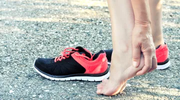A woman rubs her heel after taking off her running shoes due to heel pain